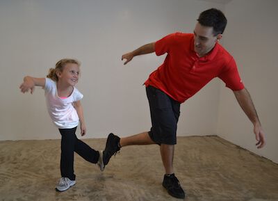 A physical therapist balancing on one foot while instructing a young girl to balance